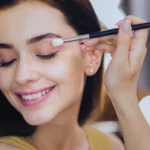 Pleasant smiling makeup artist finishing her everyday makeup